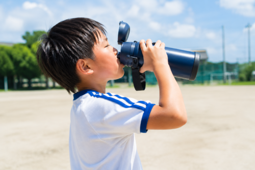 運動後に1リットル水筒で水を飲む小学生