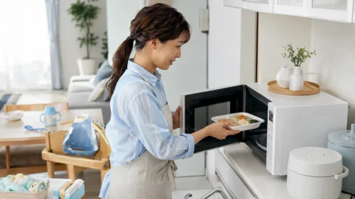 冷凍宅配弁当を電子レンジで温めて昼食を用意する保護者
